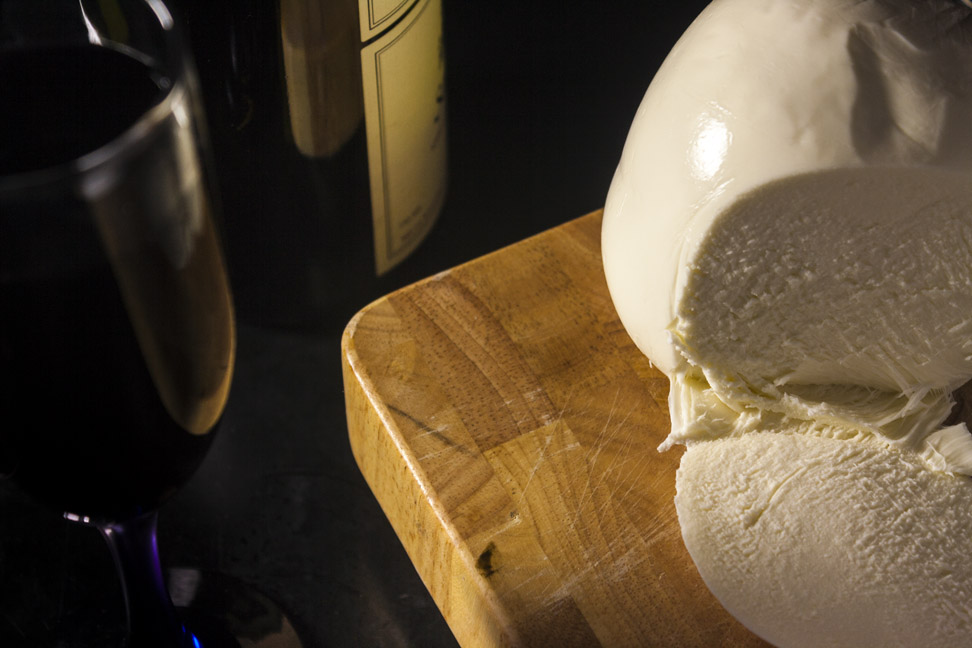 A ball of mozzarella cheese on a cutting board, a glass and a bottle of wine
